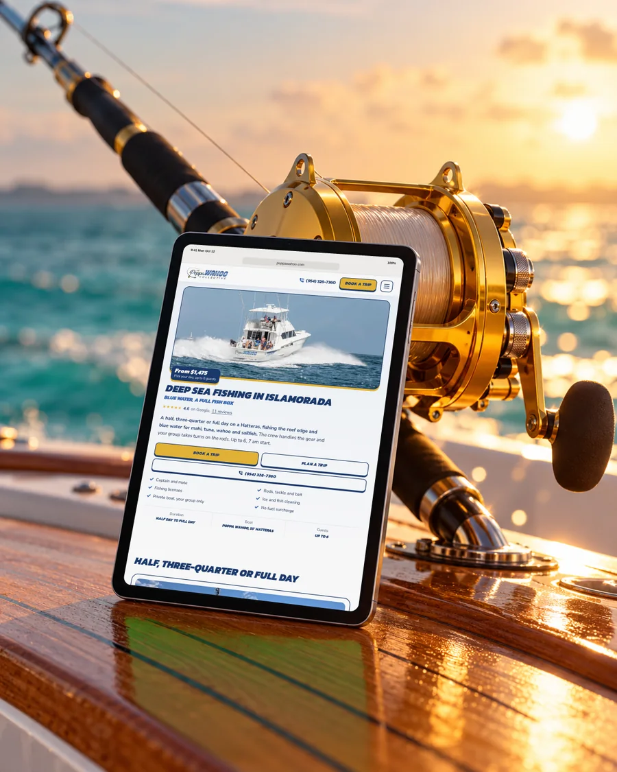 A Poppa Wahoo trip page on a tablet on a teak deck, beside a gold fishing reel at sunset